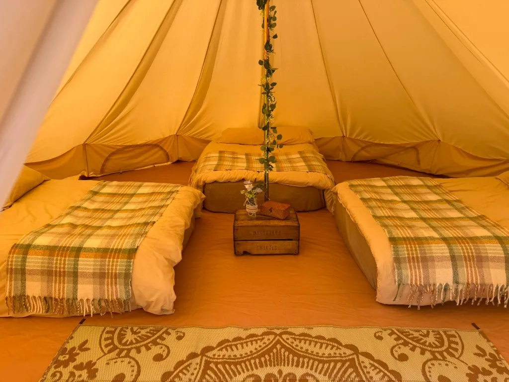 A three-bed furnished bell tent interior with plaid blankets at Woodhill Campsite, Faversham, Kent