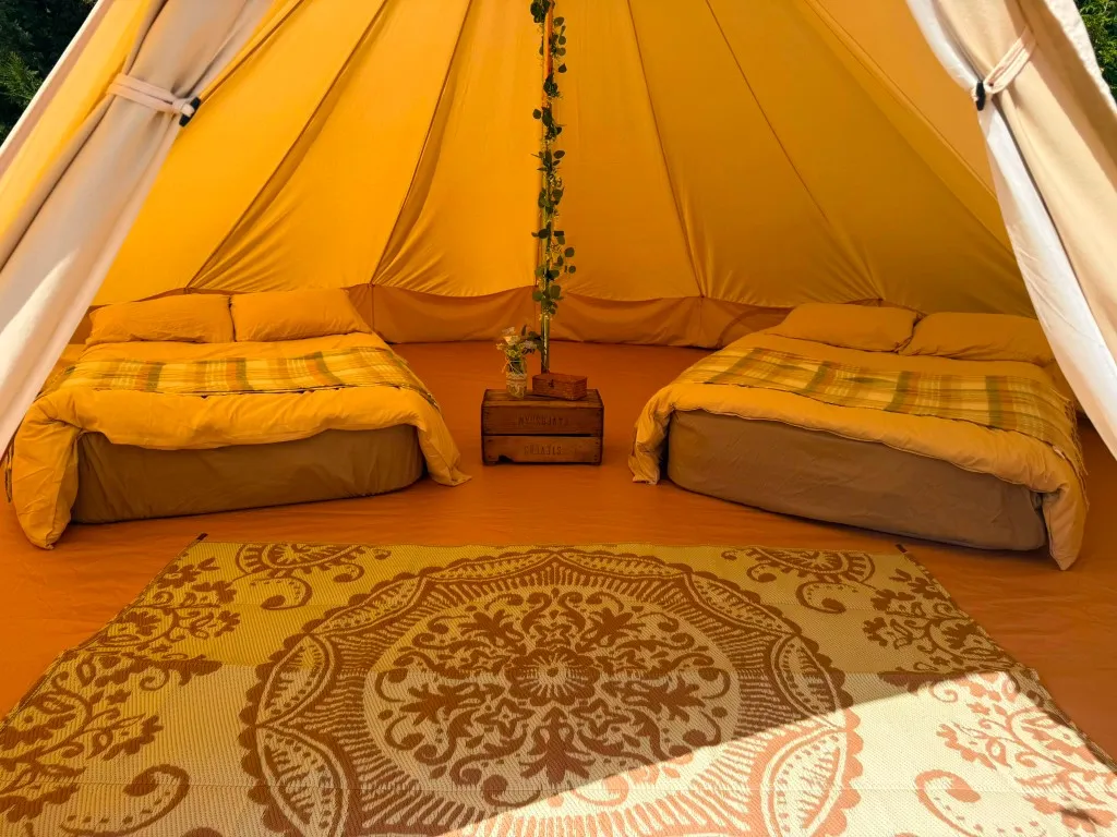 Inside a two-bed furnished bell tent with plaid throws and a mandala rug at Woodhill Campsite, Faversham, Kent