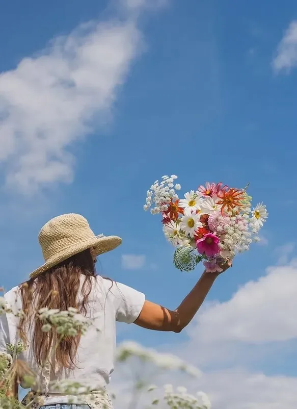Angie of Botanical Blooms holding a colourful wildflower bouquet up against a blue sky