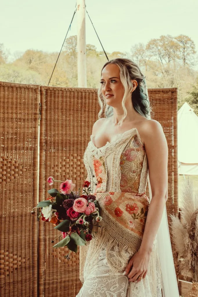 Bride holding a bouquet in front of a woven backdrop at Woodhill Weddings, Faversham, Kent