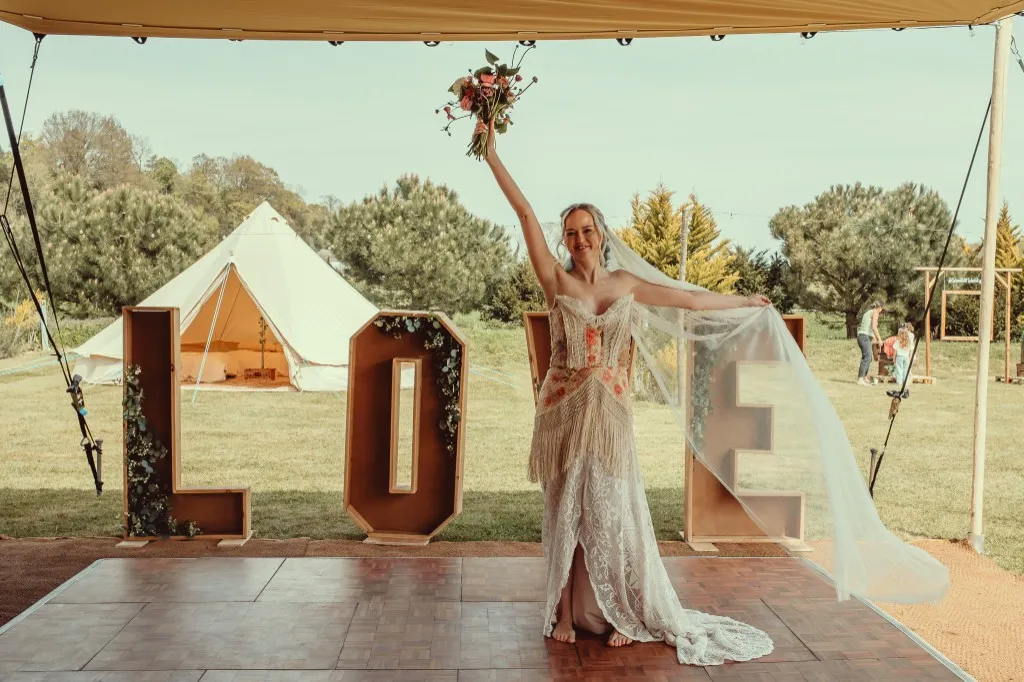 Bride celebrating on the dance floor beside giant LOVE letters at Woodhill Weddings, Faversham, Kent