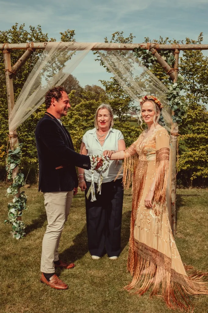 Wedding couple at a floral ceremony arch with their celebrant at Woodhill Weddings, Faversham, Kent