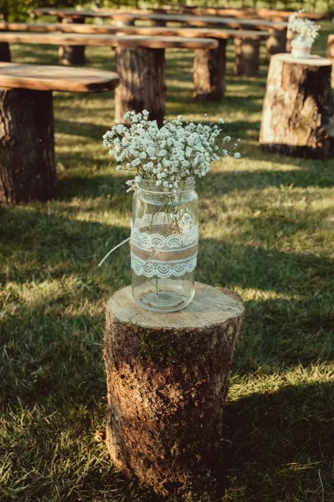 Rustic wooden ceremony benches and floral stump decor in the grounds at Woodhill Weddings, Faversham, Kent