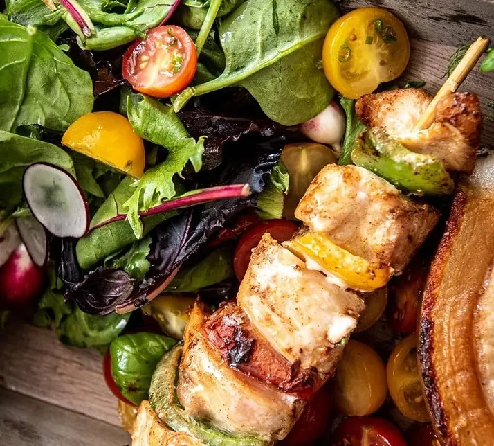 A grilled chicken kebab with peppers beside a fresh mixed salad from JD Catering Service