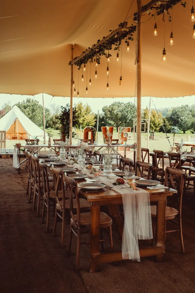 Long wooden reception tables under the stretch tent with Edison bulb lighting at Woodhill Weddings, Faversham, Kent