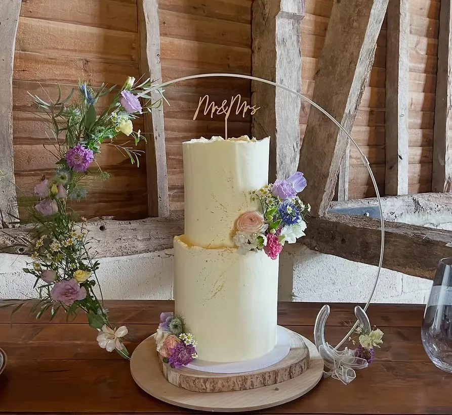 A two-tier wedding cake with gold speckles and fresh flowers from The Drip Cakery, framed by a floral hoop